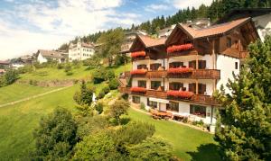 une grande maison sur une colline verdoyante avec des maisons dans l'établissement Garni Alba Bed & Breakfast, à Ortisei