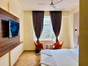 a hotel room with a bed and chairs and a tv at Hotel Nirmal's Executive in Pune