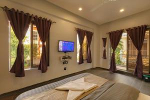 a bedroom with a bed with a tv and windows at Ragvi Resort Alibaug in Nagaon