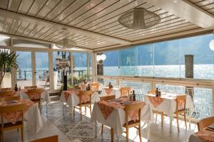 a restaurant with white tables and chairs and windows at Hotel Le Palme in Limone sul Garda