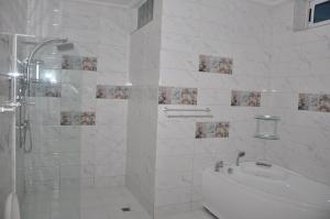 a white bathroom with a shower and a sink at Rosalie's Suites in Lomé