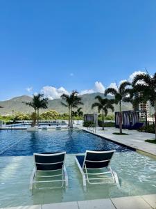 two chairs sitting next to a swimming pool with palm trees at Porto Horizonte Suite 1120 in Santa Marta