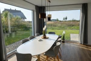 una sala da pranzo con tavolo e sedie bianchi e una grande finestra di HausLIEBLINGSPLATZ - am Meer - Luxus Villa mit 4 Schlafzimmern, 3 Badezimmern Sauna, Kamin, Weber-Grill und Wallbox a Dranske