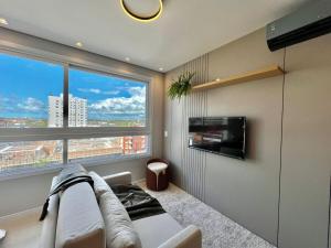 a living room with a couch and a large window at Studio Capão - novo com piscina e rooftop in Capão da Canoa