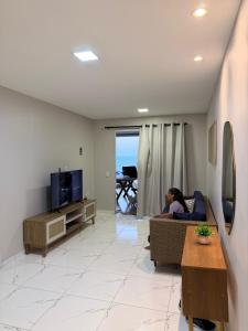 a woman sitting on a couch in a living room at Casa da Maré Pé na areia Suítes climatizadas e deck vista mar in Icapuí