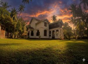 a white house with palm trees in a field at Charlotte's Coral Breeze - A Colonial Seaside Bungalow in Hikkaduwa