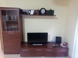 een houten tv-meubel met een televisie en een klok bij Apartamento Céntrico in Amposta