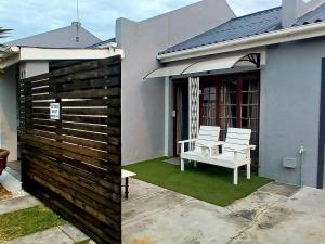 una casa con una recinzione e una panchina bianca in un cortile di Shark Cove Little Cottage a Kleinbaai