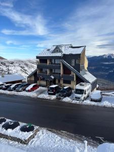 a building with cars parked in a parking lot in the snow at Résidence MAYA in Saint-Lary-Soulan