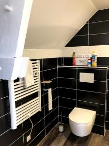 a bathroom with a toilet and a black tiled wall at Le Passiflore in Beuvron-en-Auge