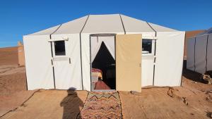 Ein Mann steht vor einem weißen Zelt in der Wüste in der Unterkunft Chegaga camp happy night in M’hamid El Ghizlane