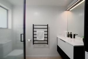 a white bathroom with a shower and a sink at Spacious, Breezy Studio Apartment, Moments from Downtown and Beach in Mount Maunganui