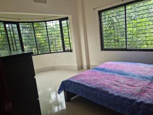 a bedroom with two large windows and a bed at M Ali House in Sylhet