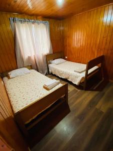 two beds in a room with wooden walls and wooden floors at La casita de Ema in Chile Chico