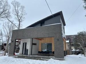 a small house with black chairs outside in the snow at Hakuba Powder Cottage Eden in Hakuba