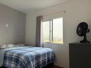 een slaapkamer met een bed en een raam met een ventilator bij Lindo apartamento completo e com garagem coberta in Palhoça