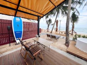 a deck with a table and a surfboard on the beach at Sichon Glamping Resort, Beachfront in Ban Plai Thon +27 photos