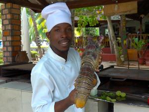 Een kok houdt een kreeft op een stok. bij Hotel Village Vacances Awale Plage in Grand-Popo