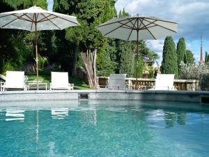 a swimming pool with two umbrellas and some chairs and tables at Villa della Pergola Relais et Chateaux in Alassio