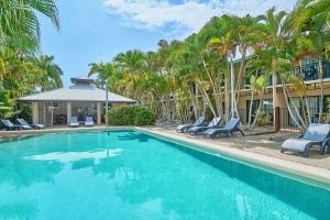 a swimming pool with chairs and palm trees at Trinity Beach Club Holiday Apartments in Trinity Beach