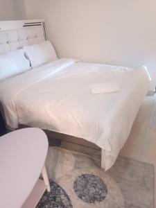 un letto con lenzuola bianche e uno sgabello in una stanza di Luxe Homes a Meru