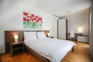 un dormitorio con una cama blanca y una pintura de flores rojas en Apartments Poville Residence en Povile