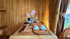 a wooden table with two cups and plates on it at Wana Bamboo House by ecobreeze in Sidemen