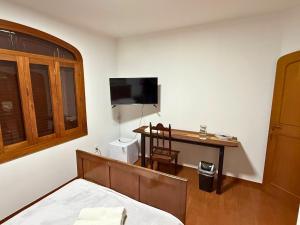 a bedroom with a bed and a desk with a television at Villa Ipe in Patos de Minas