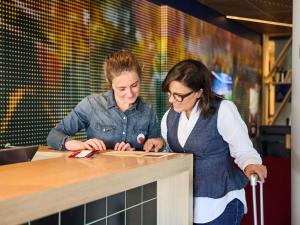 Zwei Frauen stehen an einem Tresen und schauen etwas an. in der Unterkunft Ibis Alcala de Henares La Garena in Alcalá de Henares