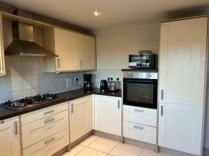 a kitchen with white cabinets and a stove top oven at Chartsworth 4 Bedrooms Spacious House in Harold Wood