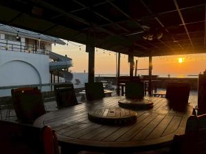 a wooden table and chairs on a deck with the sunset at บ้านดาริน บีช Baan Darlin Beach in Phetchaburi