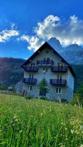 a building in a field of grass with mountains in the background at Sunhouse Valbone in Valbonë