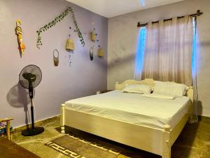 a bedroom with a bed with white sheets and a fan at HIGSAM apartment in Diani Beach