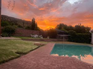 a swimming pool with a sunset in the background at De Kleine Kaap Guesthouse in Lady Grey