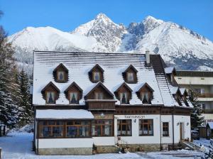 a large building with snow covered mountains in the background at Penzión Encián in Tatranská Lomnica