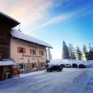 een gebouw met auto's buiten geparkeerd in de sneeuw bij Bar-Restaurant-Pizzeria Antermont B&B in Carezza al Lago