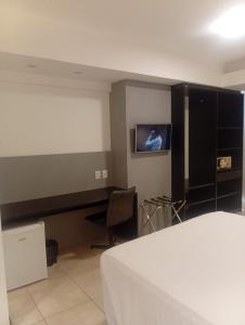 a bedroom with a bed and a desk and a tv at Suítes Executivas in Feira de Santana