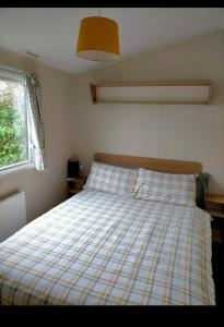een slaapkamer met een bed met een geruite deken bij Sycamores Caravan in Helston