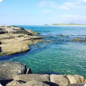 a large body of water with rocks and blue water at Varanda Praiana in Rio das Ostras