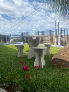 three white benches sitting in the grass with flowers at Suíte privativa quarto in Xaxim +4 photos