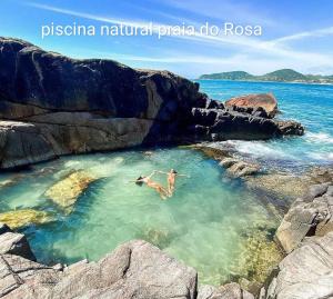 two people swimming in the water near a rocky beach at Loft e casa Catarina in Imbituba +7 photos