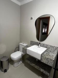 a bathroom with a toilet and a sink and a mirror at Quarto standard 9 in Guarapari