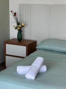 a bed with two rolled towels and a vase with flowers at Quarto standard 9 in Guarapari