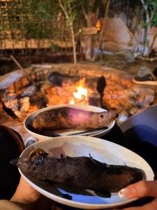 a person holding two plates of food in front of a fire at Shasha Siwa Retreat & Thermal Spring in Siwa