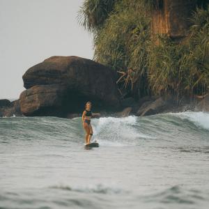 a woman riding a wave on a surfboard in the ocean at Nirvana Surf Retreat - Kabalana in Atadahewatugoda +13 photos