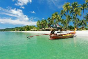 a boat in the water on a beach with palm trees at Mook Phoopha Guest House in Ko Mook