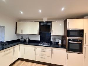 a kitchen with white cabinets and black counter tops at Sleek Modern 2BDR Flat in Charming Pinner in Northwood +5 photos