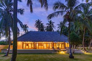 a house with a thatched roof and palm trees at Villa Madu Mentawai in Katiet
