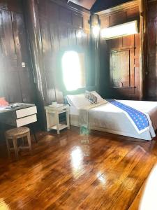 a bedroom with a bed and a desk and wooden floors at Niyang Siam House in Nai Yang Beach