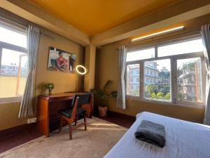 a bedroom with a desk and a bed and windows at Sunny Side Up top-floor apartment in Kathmandu